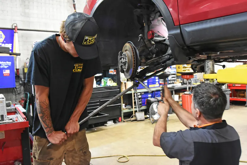 Two technicians repairing the front brakes and suspension of an SUV raised on a lift
