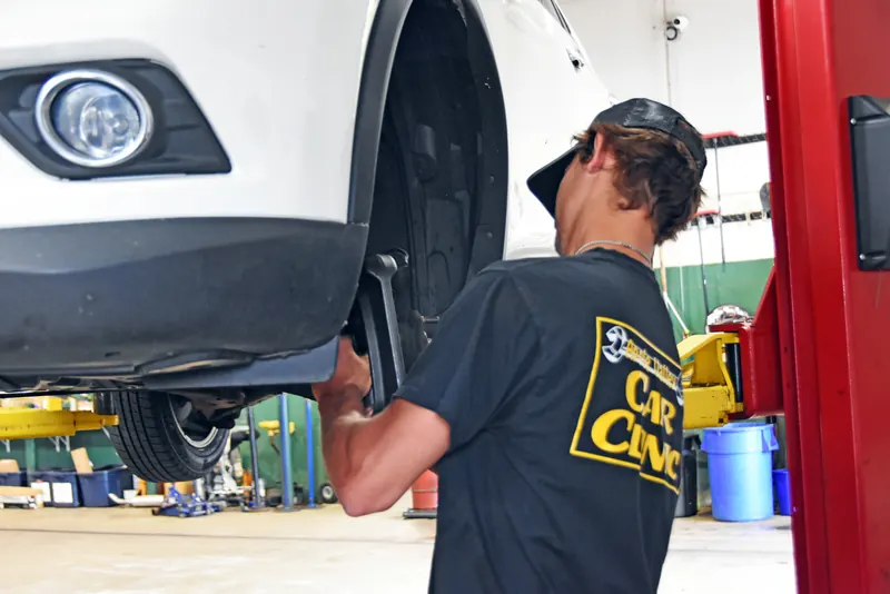 Technician working on the front wheel and brake area of a white SUV on a lift