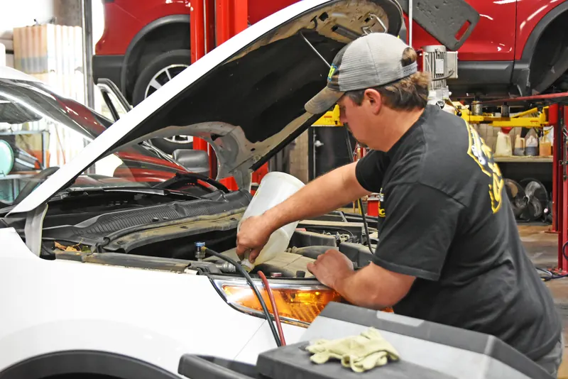 Technician adding fluid under the hood of a white SUV in the service bay